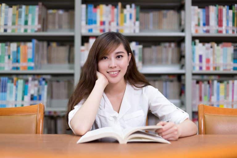Beautiful asian female student read book in library with bookshe